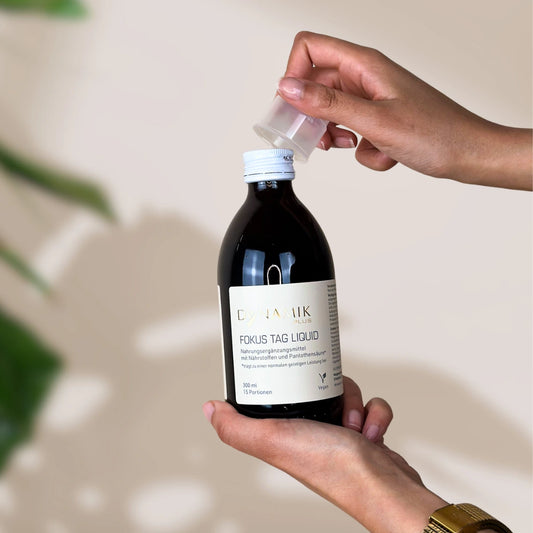 Braune Flasche mit DynamikPlus "Fokus Tag Liquid" Etikett und kleinem Messbecher auf Verschluss