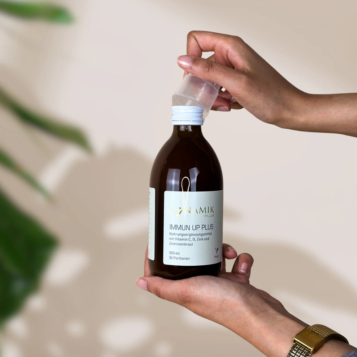 Braune Flasche mit DynamikPlus "Immun Up Plus" Etikett und kleinem Messbecher auf Verschluss