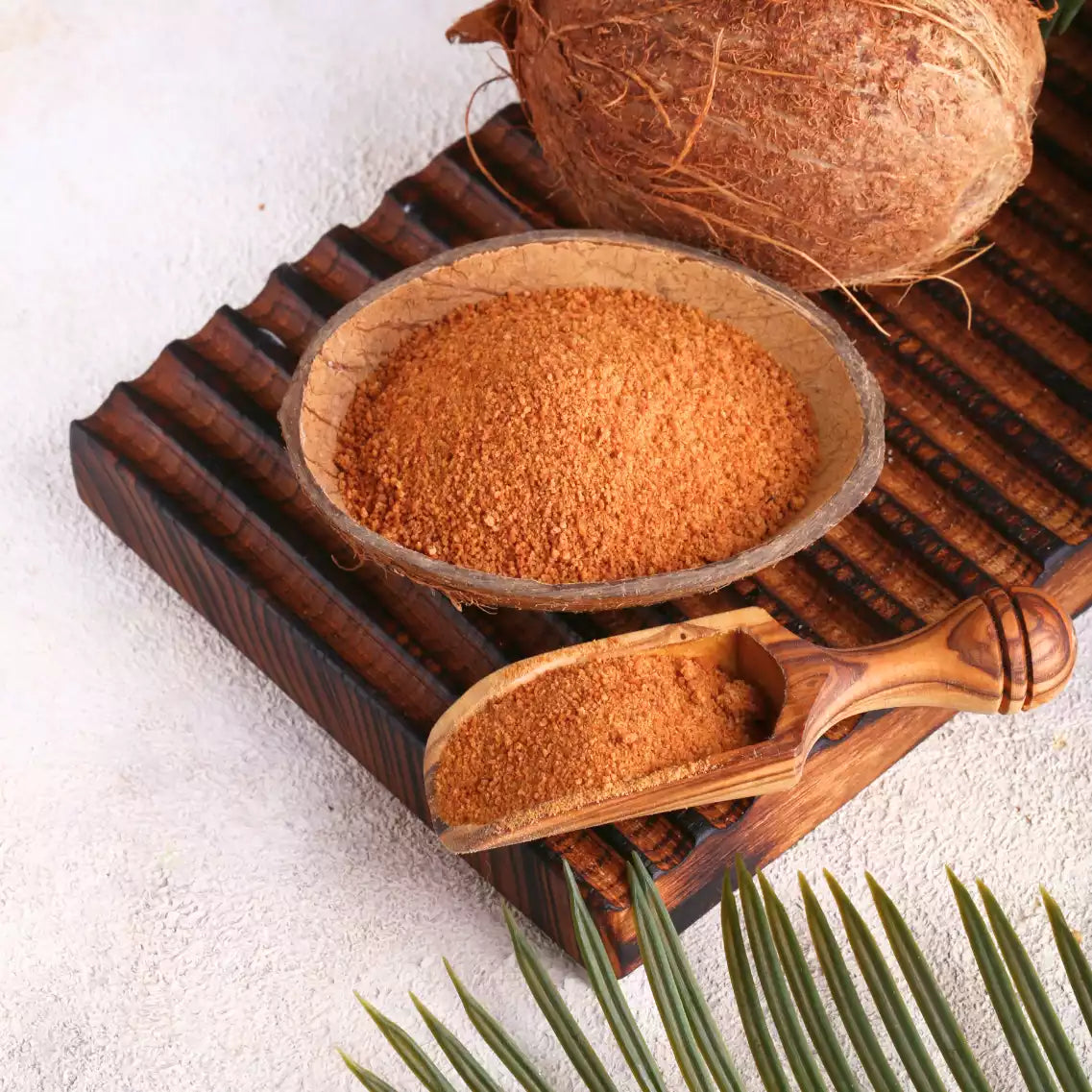 Kokosblütenzucker in Schale mit Holzschaufel auf Holzbrett im Sand