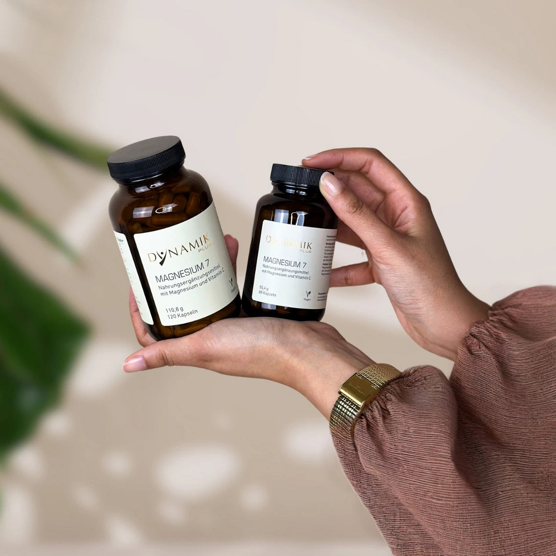 Brauner Glasbehälter mit DYNAMIKPLUS Etikett "Magnesium 7" in 2 verschiedenen Größen, gehalten von einer Hand