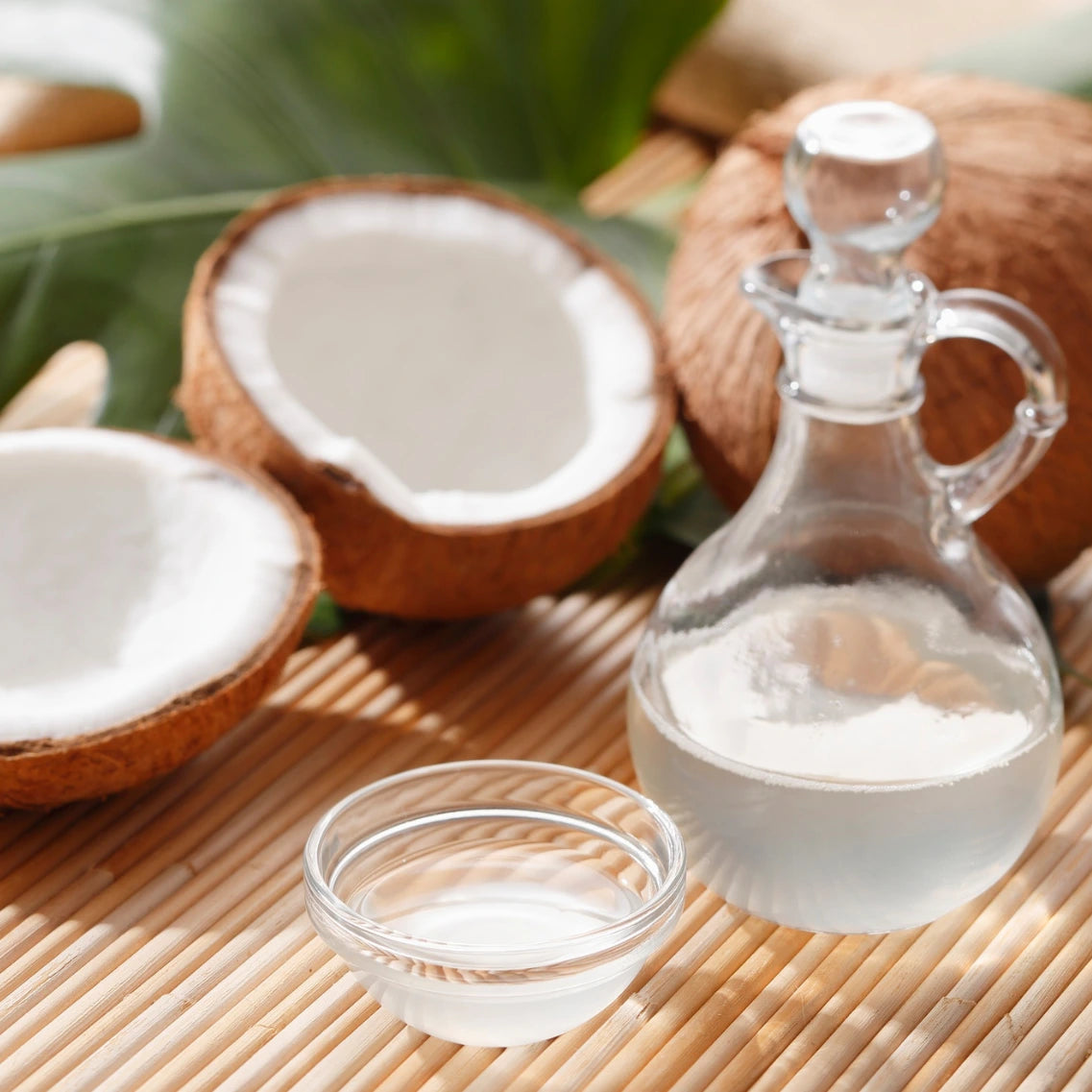 Kokosnussöl in Karaffe und kleiner Schüssel mit Kokosnüssen im Hintergrund