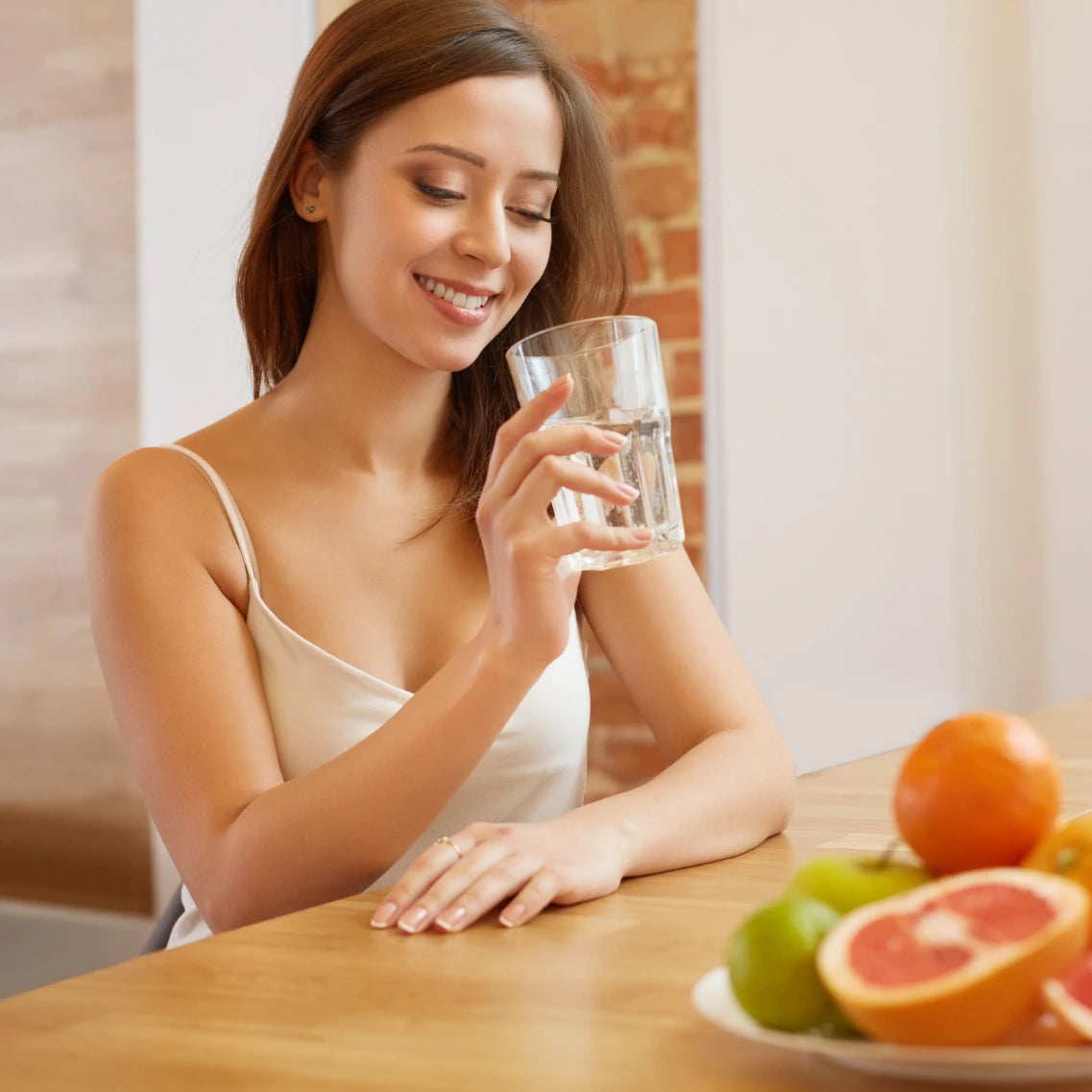 Frau mit Glas Wasser in der Hand und einer Früchteschale auf dem Tisch