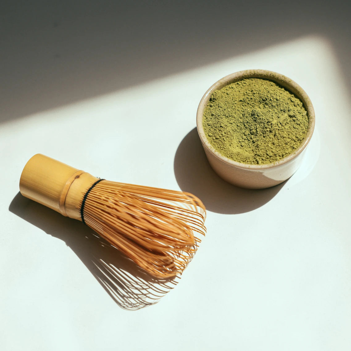 Matcha Besen und kleine Schale gefüllt mit Matcha auf weißem Hintergrund