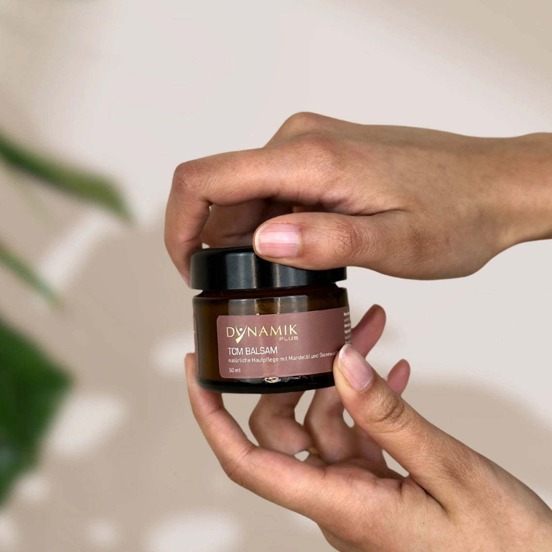 Brauner Glasbehälter in Händen gehalten mit DYNAMIKPLUS Etikett "TCM Balsam"