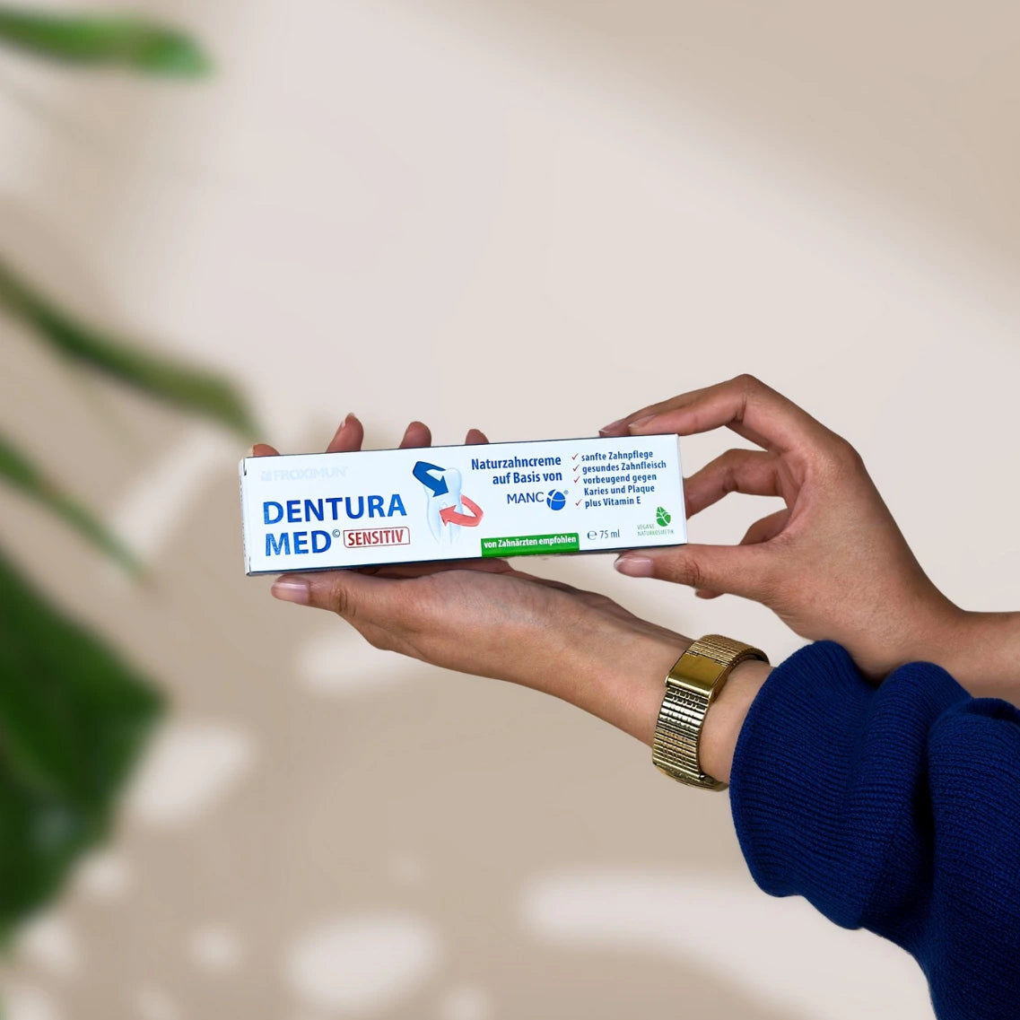 Rechteckige weiß-blaue Verpackung mit "Froximun DENTURA MED" Print und Zahn auf Verpackung, gehalten