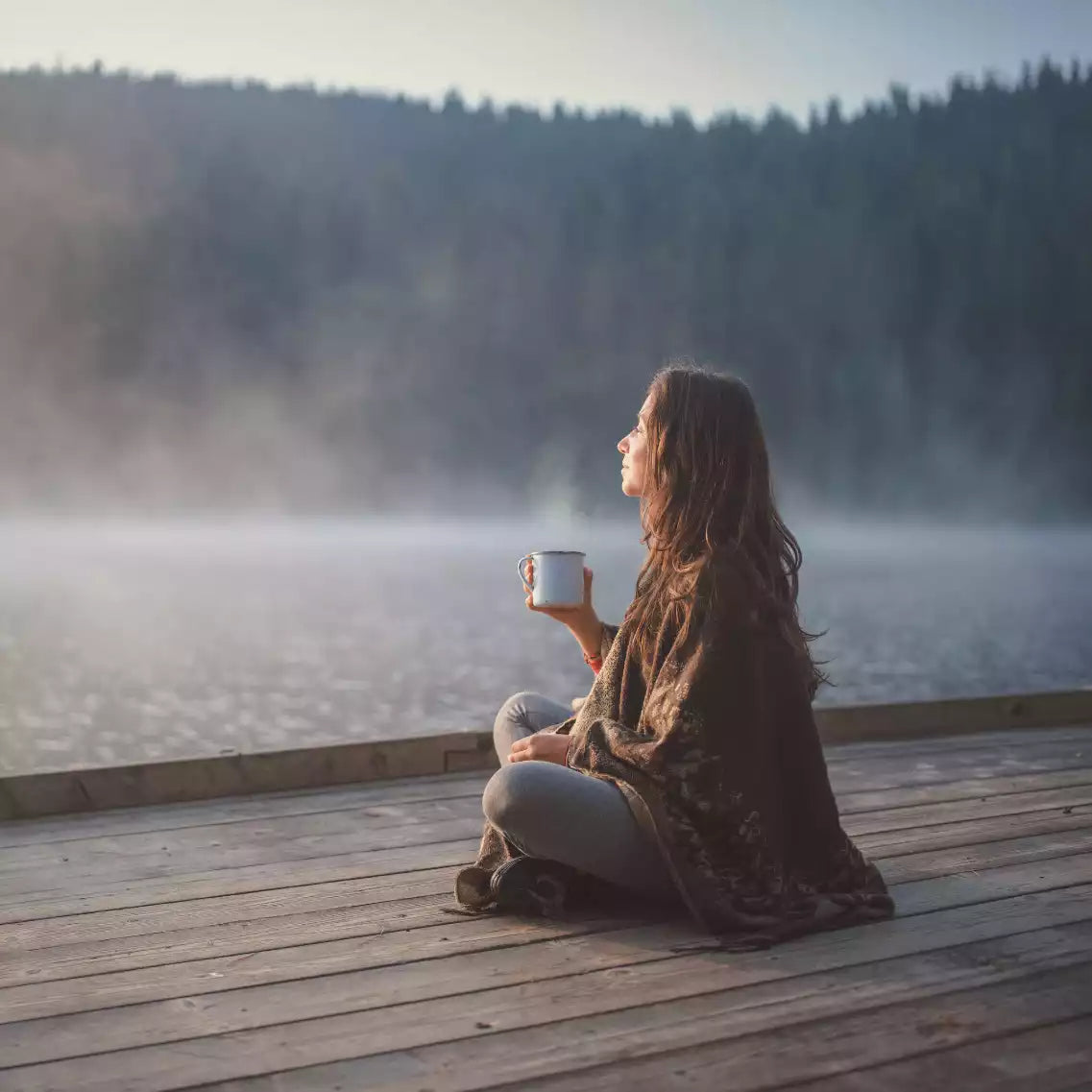 Frau mit Tasse in der Hand sitzend an Steg