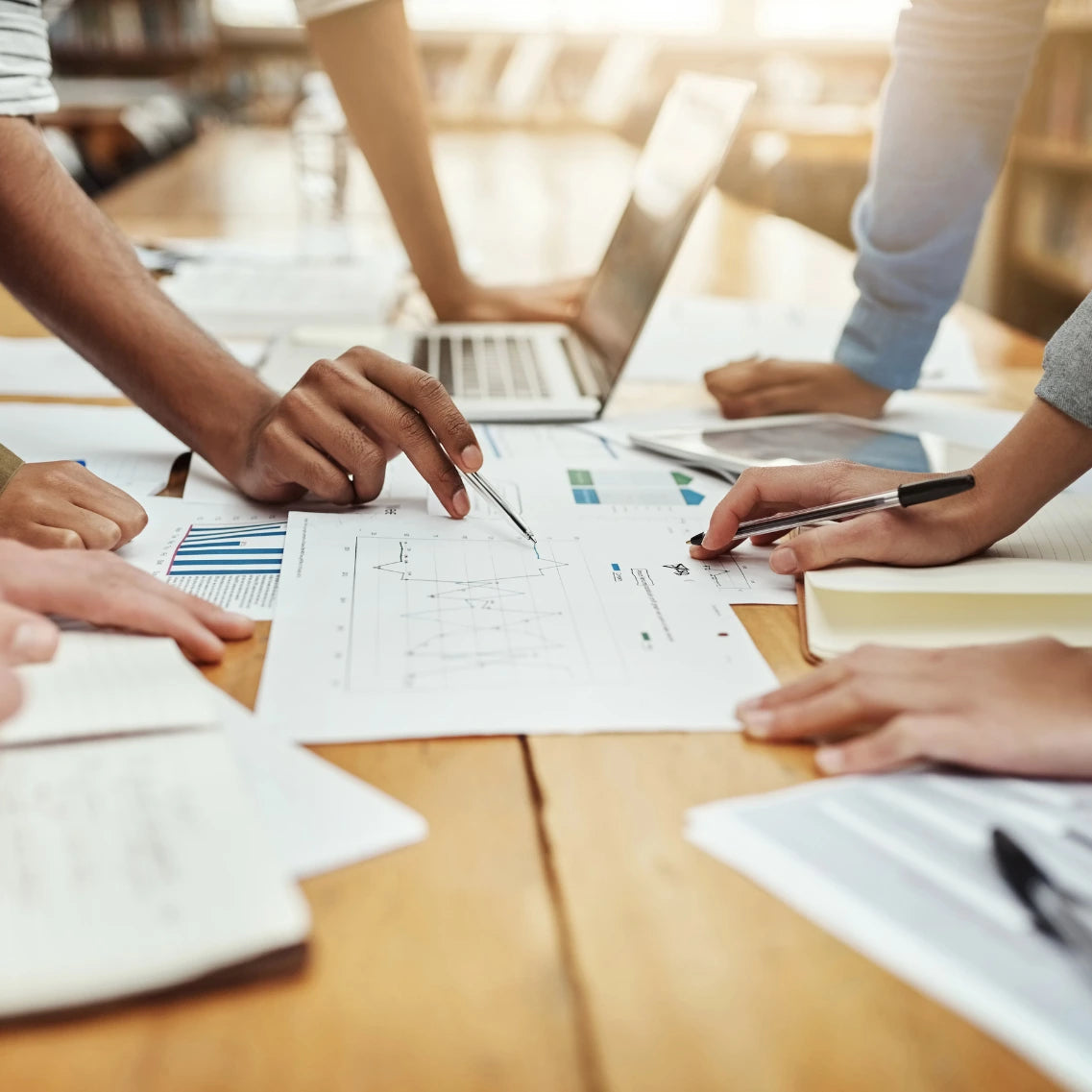 Arbeitstisch mit Dokumenten, Laptop und analysierenden Leuten