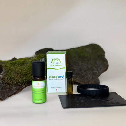 Schwarze Platte und Armband, kleines Fläschchen, größeres Fläschchen mit "Grapefruit Bio" Etikett und weiße Verpackung mit grünem aromaveda Druck