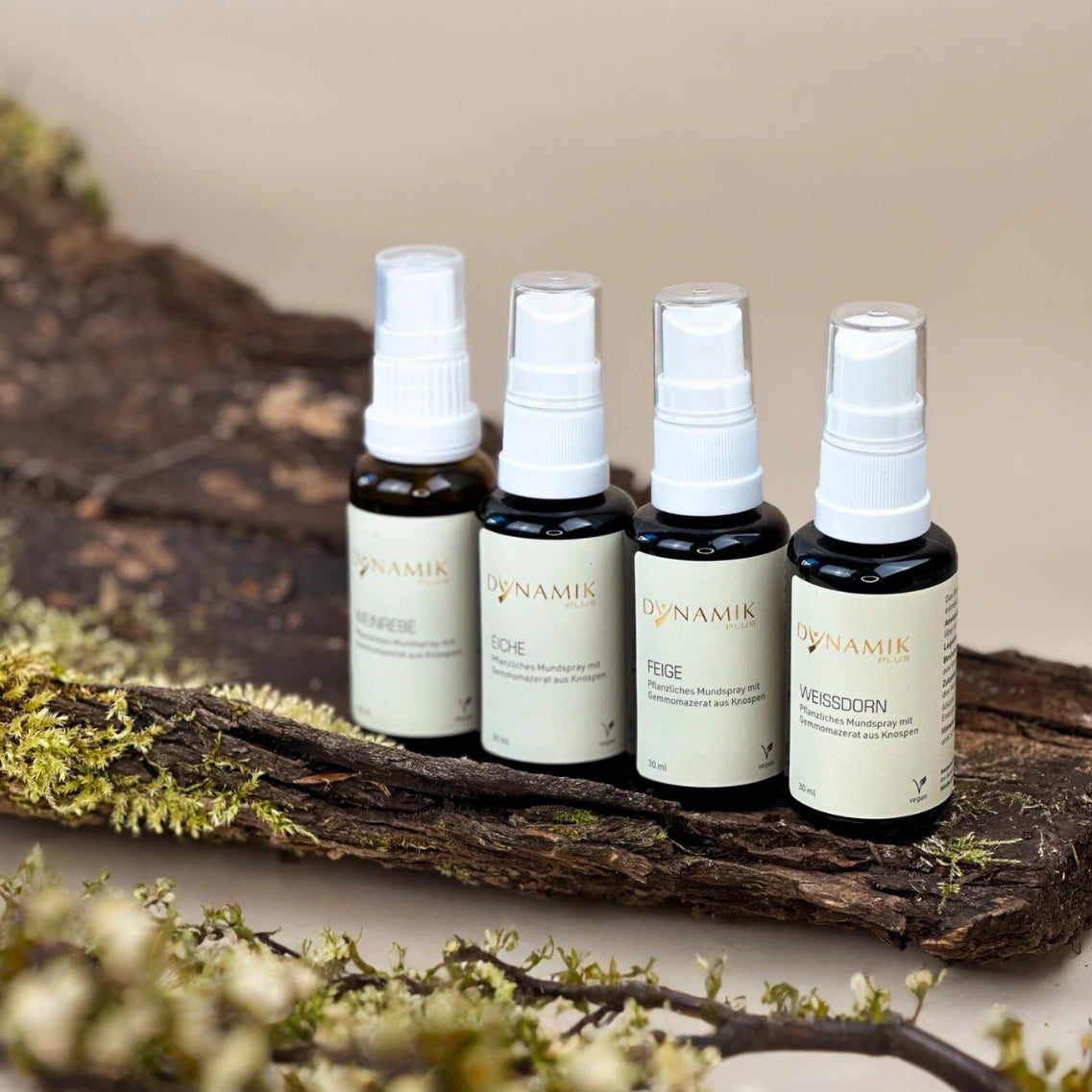 4 braune Sprühfläschchen mit weißem Sprühkopf und DynamikPlus Etikett angereiht auf einem Ast