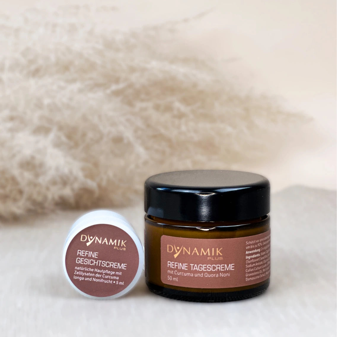 Kleiner runder weißer Plastikbehälter und braunes größeres Glasbehältnis mit jeweils DynamikPlus "Refine Tagescreme" Etikett