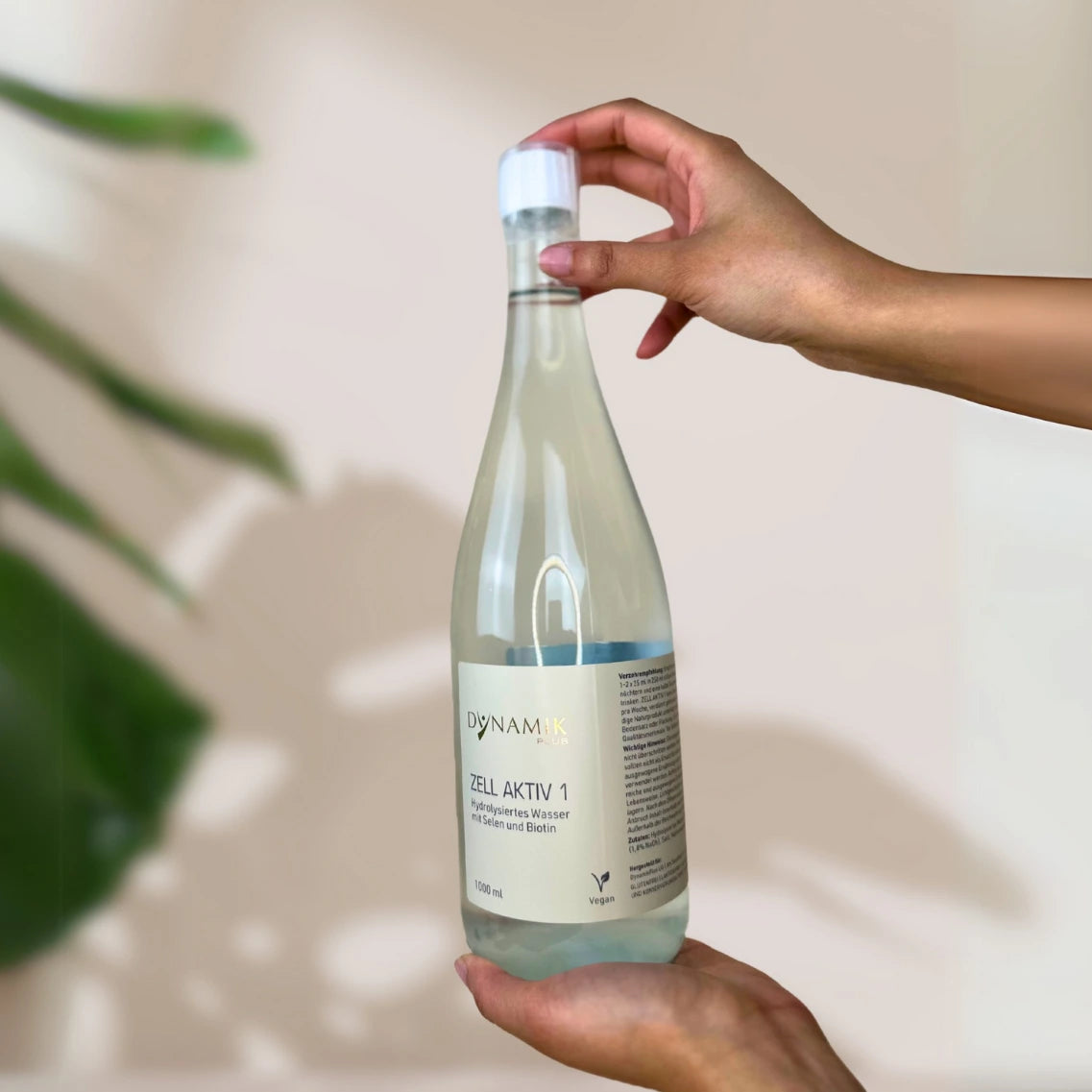 Glasflasche mit weißem Deckel, kleinem Messbecher und DynamikPlus "Zell Aktiv 1" Etikett gehalten von zwei Händen