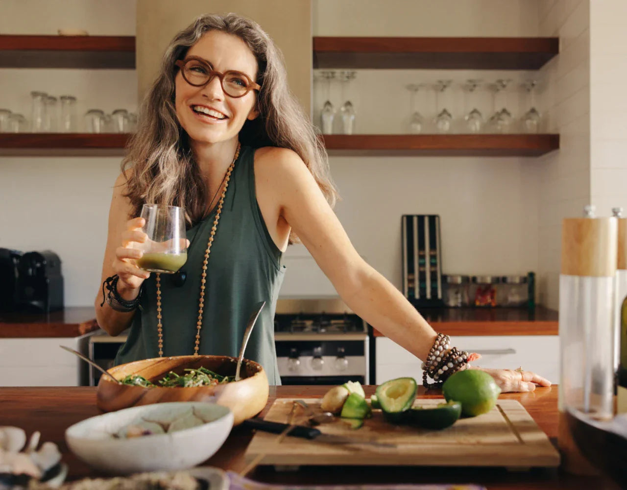 Frau in Küche mit Glas Saft in der Hand und einer Schüssel Salat vor sich